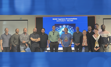 the first cohort of SEAM participants stand as a group in front of a large video screen